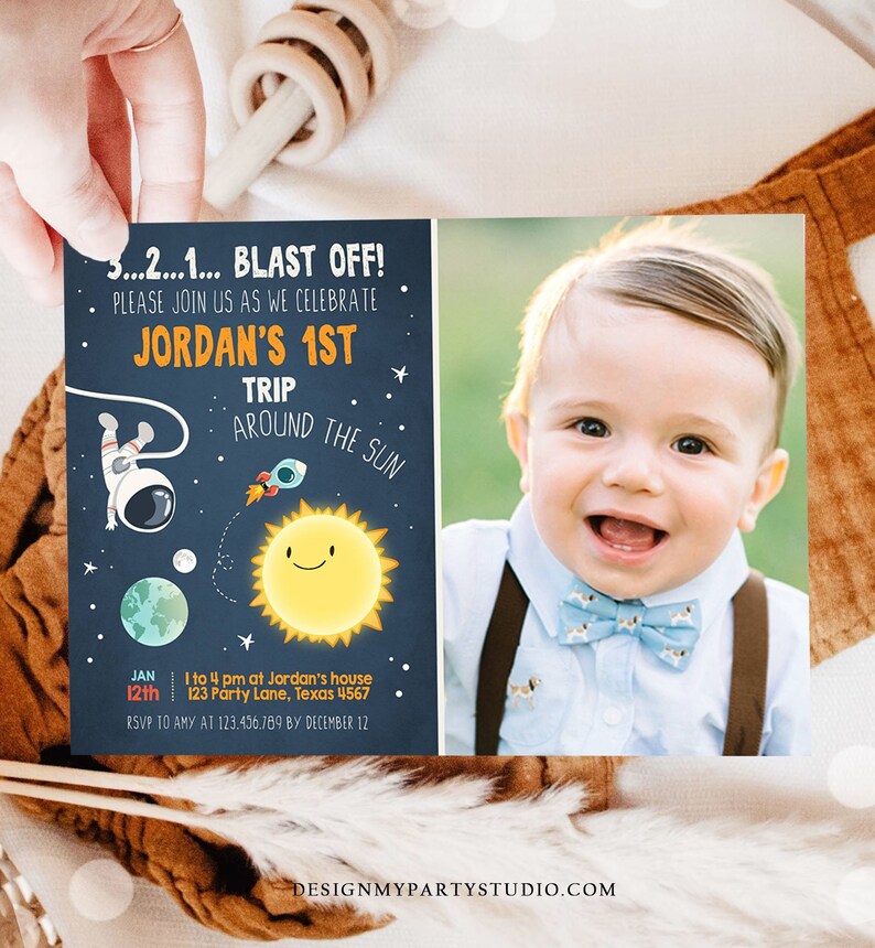 May include: A blue and orange space-themed first birthday party invitation with a photo of a baby boy wearing a bow tie. The invitation says "3...2...1... BLAST OFF! Please join us as we celebrate Jordan's 1st Trip Around the Sun" and includes the date, time, and location of the party.