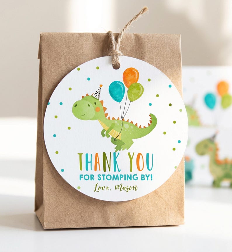 May include: A round white paper gift tag attached to a brown paper bag with twine. The tag features a green dinosaur wearing a party hat, holding orange, blue, and green balloons, with the text THANK YOU FOR STOMPING BY! Love, Mason.