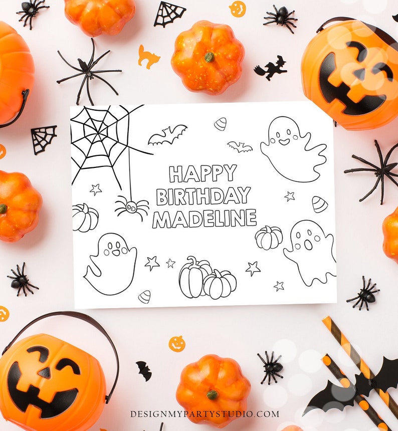 May include: A Halloween-themed birthday card with the text "Happy Birthday Madeline" surrounded by pumpkins, spiders, bats, and ghosts. The card is black and white, with orange and black decorations scattered around it.
