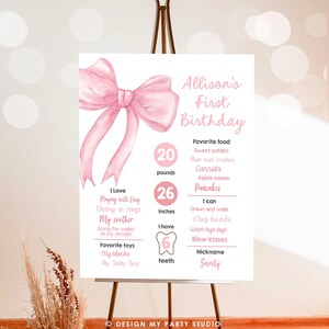 May include: Pink and white first birthday milestone poster with a large pink bow at the top. The poster lists the child's age, weight, height, number of teeth, favorite foods, and things they can do. The poster is titled "Allison's First Birthday".
