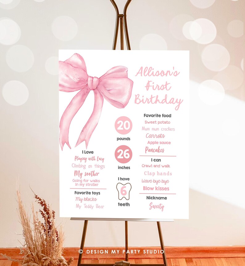 May include: Pink and white first birthday milestone poster with a large pink bow at the top. The poster lists the child's age, weight, height, number of teeth, favorite foods, and things they can do. The poster is titled "Allison's First Birthday".