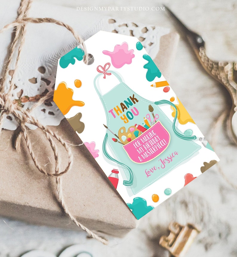 May include: A gift tag with a light blue apron design, featuring the words "Thank You" and "For making my birthday a masterpiece!" with the name "Jessica". The tag is decorated with paint splatters and art supplies.