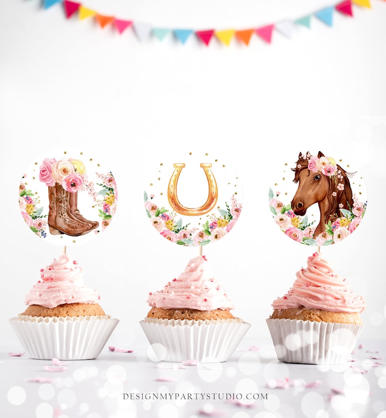 May include: Three pink cupcakes with white wrappers topped with pink frosting. Each cupcake has a round, white paper topper with a different design: a pair of brown cowboy boots with pink flowers, a gold horseshoe with pink flowers, and a brown horse with a pink flower crown.