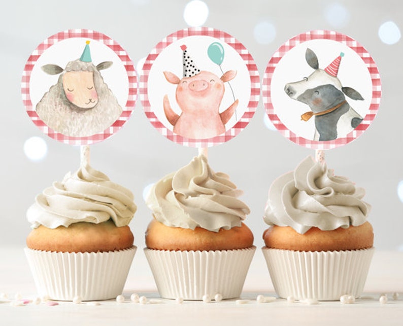 May include: Three cupcakes decorated with red and white gingham patterned circles featuring a pig, a cow, and a sheep. The cupcakes are topped with white frosting.