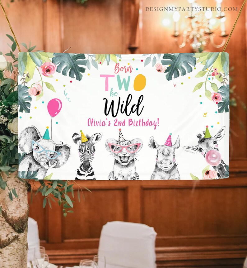 Peut inclure: Une banni&egrave;re blanche sur le th&egrave;me de la jungle pour un deuxi&egrave;me anniversaire. La banni&egrave;re dit "Born Two Be Wild" avec un sch&eacute;ma de couleurs rose, jaune et vert. La banni&egrave;re repr&eacute;sente un z&egrave;bre, un &eacute;l&eacute;phant, un lion et un rhinoc&eacute;ros portant des chapeaux de f&ecirc;te.