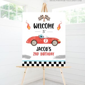 May include: Welcome to Jacob's 2nd Birthday sign featuring a red race car with a checkered flag and flames. The sign has a black and white checkered border.