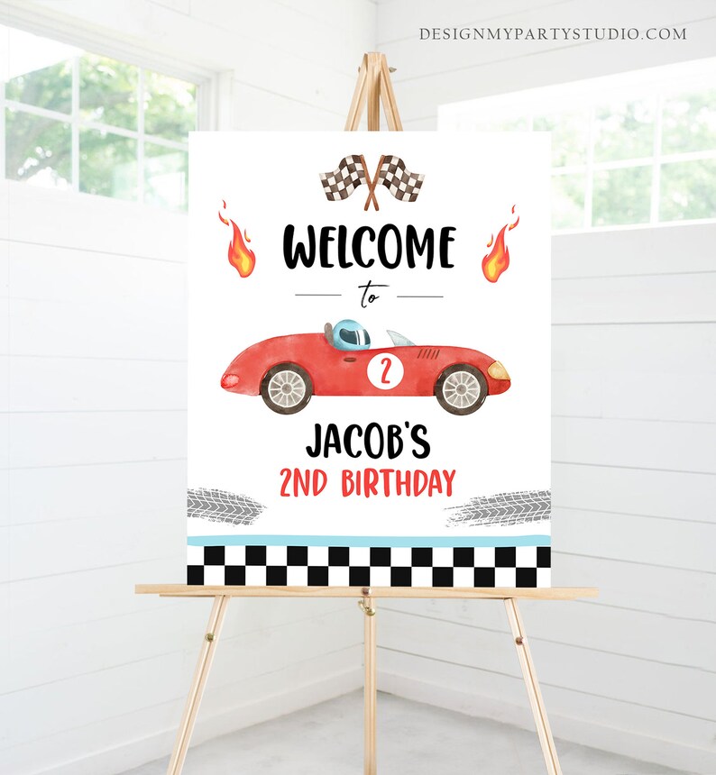 May include: Welcome to Jacob's 2nd Birthday sign featuring a red race car with a checkered flag and flames. The sign has a black and white checkered border.