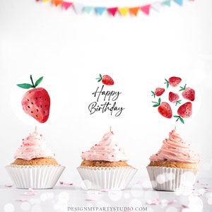 K&ouml;nnte beinhalten: Drei rosa glasierte Cupcakes mit wei&szlig;en Cupcake-F&ouml;rmchen. Jeder Cupcake hat einen runden, wei&szlig;en Papier-Topper mit einem Aquarell-Erdbeer-Design. Der mittlere Topper sagt "Happy Birthday" in schwarzer Schrift.