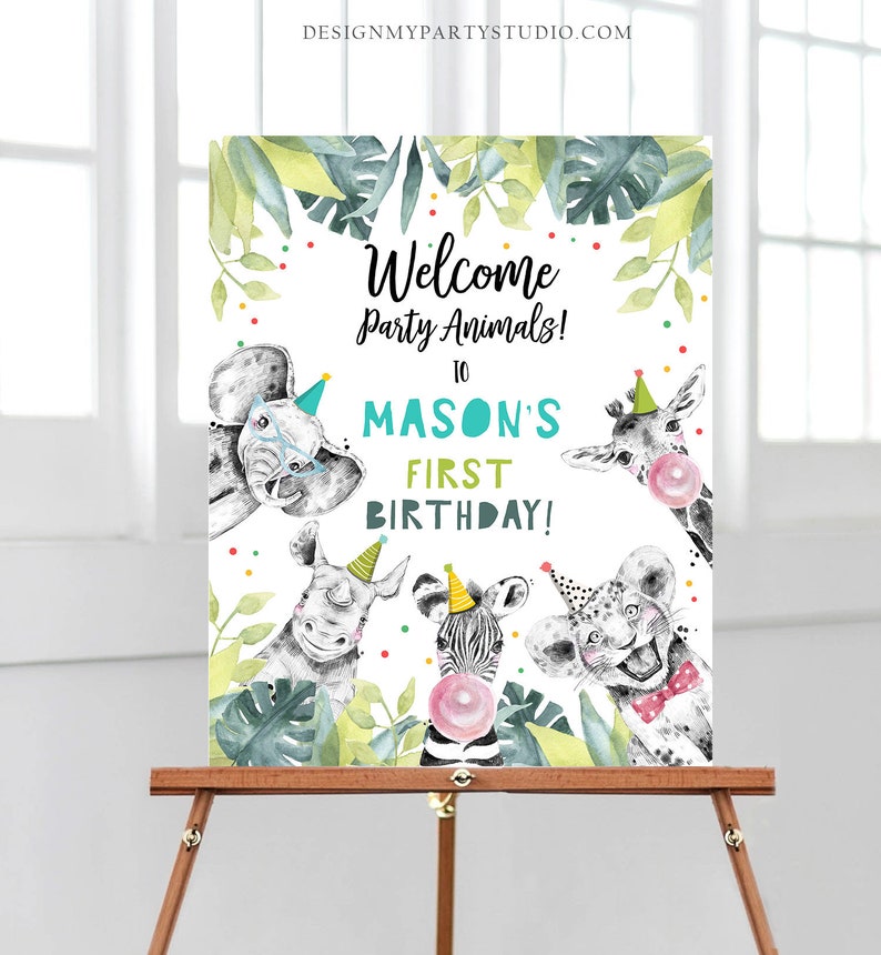 May include: Welcome to Mason's First Birthday party sign with a jungle theme. The sign features a white background with colorful confetti and green leaves. There are five animals peeking out from behind the leaves, including an elephant, a giraffe, a rhino, a zebra, and a lion. The animals are all wearing party hats and have playful expressions.