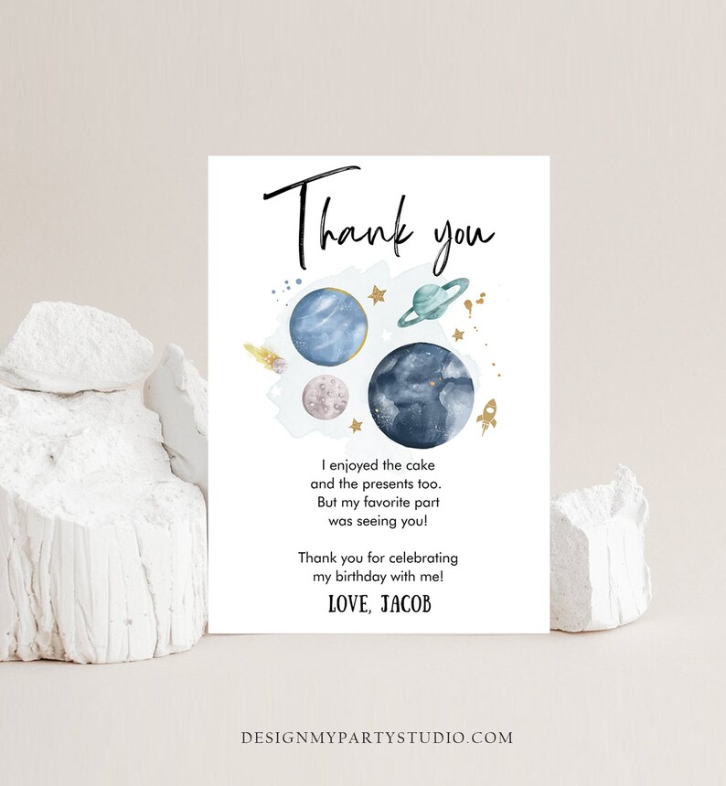 May include: A white thank you card with a space-themed design. The card features illustrations of planets, stars, and a rocket. Text includes "Thank you", a personal message, and "LOVE, JACOB". The card is designed for a birthday celebration.