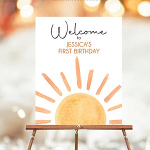 以下が含まれることがあります： ジェシカの1歳の誕生日へようこそサイン。白い背景にオレンジ色の光線が描かれた水彩画の太陽が描かれています。