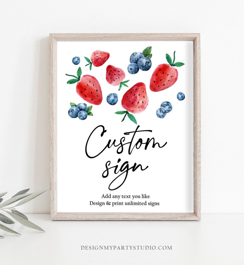 May include: A white sign with the text "Custom sign" in black cursive font. The sign is decorated with watercolor illustrations of red strawberries and blue blueberries. The text "Add any text you like" and "Design & print unlimited signs" is also included on the sign. The sign is framed in a light wood frame.