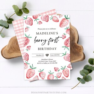 May include: A pink and white gingham patterned background with a white card featuring a watercolor illustration of strawberries. The card is a birthday invitation for Madeline's first birthday. The text on the card reads "Please join us to celebrate Madeline's berry first birthday. October 22 from 4:00 PM. Madeline's House 123 Party Lane, Texas 4567. RSVP to Ashley at 123.456.789. Designmypartystudio.com."
