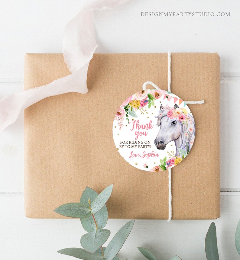 Puede incluir: Un regalo envuelto en papel marr&oacute;n con una etiqueta decorativa. La etiqueta presenta un caballo blanco con una corona floral y el texto "Thank you for riding on by to my party! Love, Sophia."