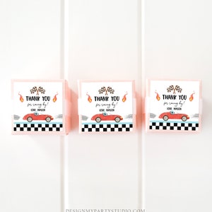 Op de afbeelding: Drie roze cadeaudoosjes met witte etiketten. De etiketten tonen een rode raceauto, een geblokte vlag en vlammen. De tekst op de etiketten luidt "Bedankt voor het racen! Liefs, Mason".