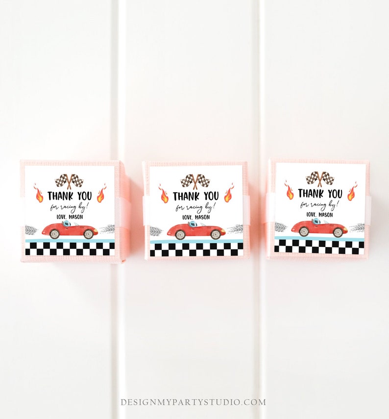 Op de afbeelding: Drie roze cadeaudoosjes met witte etiketten. De etiketten tonen een rode raceauto, een geblokte vlag en vlammen. De tekst op de etiketten luidt "Bedankt voor het racen! Liefs, Mason".