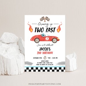 May include: A red race car with a checkered flag and flames on either side. The text "Growing up TWO FAST" is above the car. The text "Join us to celebrate JACOB'S 2ND BIRTHDAY" is below the car. The text "OCTOBER 17TH 4:00 - 6:00 PM JACOB'S HOUSE 123 PARTY LANE, TEXAS 4567 RSVP TO ASHLEY AT 123.456.789" is below the car. The text "DESIGNMYPARTYSTUDIO.COM" is at the bottom of the invitation.