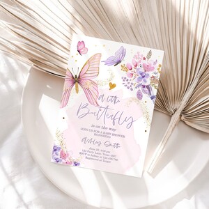 K&ouml;nnte beinhalten: Eine rosa und violette Babyparty-Einladung mit goldenem Glitzerhintergrund. Die Einladung zeigt einen Schmetterling mit goldenen Akzenten und den Text "A little Butterfly is on the way".