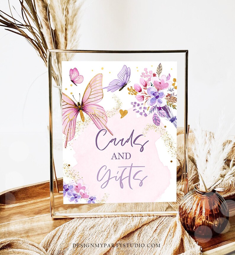 May include: A printable sign with a pink watercolor background and gold glitter accents. The sign says "Cards and Gifts" in purple script with butterflies and flowers in the background.