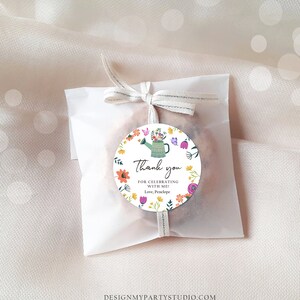 May include: A round thank you favor tag with a colorful floral design and a green watering can. The tag says "Thank you for celebrating with me! Love, Penelope".