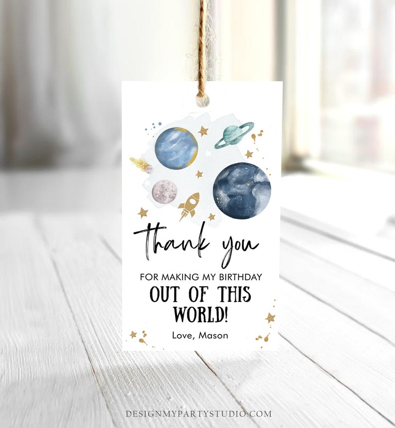 May include: A white thank you tag with a blue and gold space theme. The tag features planets, stars, and a rocket ship. The text on the tag reads "Thank you for making my birthday out of this world! Love, Mason".