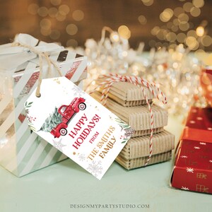 Puede incluir: Una etiqueta de regalo navide&ntilde;a con un cami&oacute;n rojo vintage que lleva un &aacute;rbol de Navidad, con las palabras "Happy Holidays!" y "From The Smith's Family". La etiqueta est&aacute; atada a un regalo envuelto con hilo.