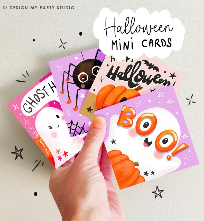 May include: A hand holds a stack of Halloween mini cards. Each card features a different spooky illustration, including a ghost, spider, and pumpkin. The cards are in shades of pink, purple, and orange, with the words "Halloween" and "BOO" written on them.
