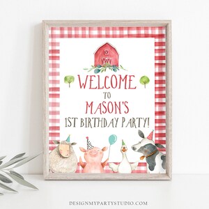 May include: A red and white gingham welcome sign for a farm-themed first birthday party. The sign features a red barn, a sheep, a pig, a goose, and a cow. The text on the sign reads "Welcome to Mason's 1st Birthday Party!"