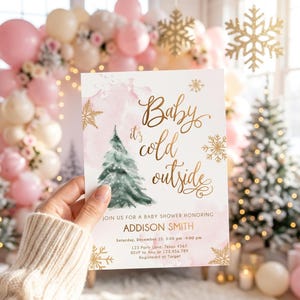 May include: A rectangular baby shower invitation card featuring a watercolour pink background, a green pine tree illustration, and gold foil-style snowflakes. The text reads: Baby it's cold outside, JOIN US FOR A BABY SHOWER HONORING ADDISON SMITH.