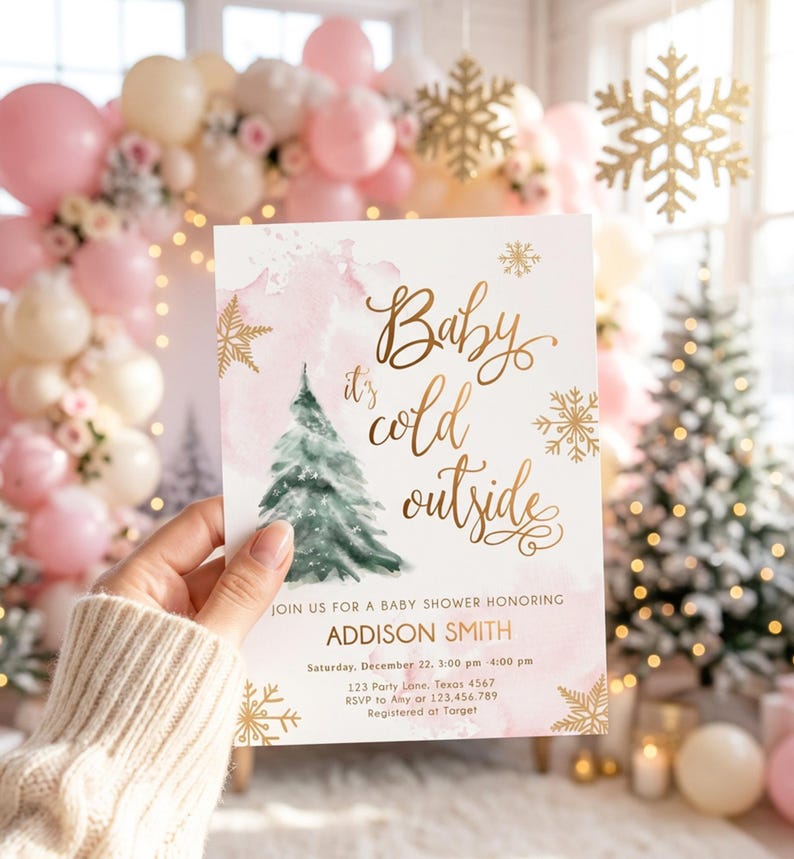 May include: A rectangular baby shower invitation card featuring a watercolour pink background, a green pine tree illustration, and gold foil-style snowflakes. The text reads: Baby it's cold outside, JOIN US FOR A BABY SHOWER HONORING ADDISON SMITH.