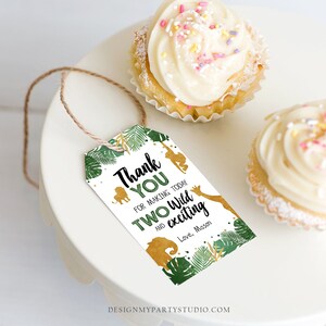 May include: A white tag with a jungle theme, featuring the text "Thank You for making today TWO Wild and exciting". The tag includes gold animal silhouettes and green foliage. Two cupcakes with white frosting and sprinkles are also visible.