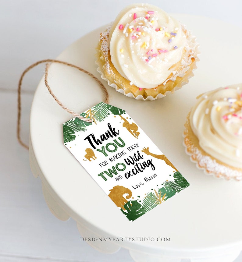May include: A white tag with a jungle theme, featuring the text "Thank You for making today TWO Wild and exciting". The tag includes gold animal silhouettes and green foliage. Two cupcakes with white frosting and sprinkles are also visible.