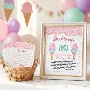 May include: A framed sign titled Time Capsule with ice cream graphics and text for Olivia, alongside a wicker basket filled with matching lined cards featuring pink icing and sprinkle designs, all set against a backdrop of colorful party balloons.