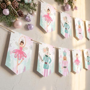 Peut inclure: Une guirlande décorative composée de fanions en papier blanc en forme de pointe, illustrés de ballerines en tutu rose, de souris soldats en uniforme bleu sarcelle et de casse-noisettes en tenues roses et bleu sarcelle, suspendus sur une ficelle.