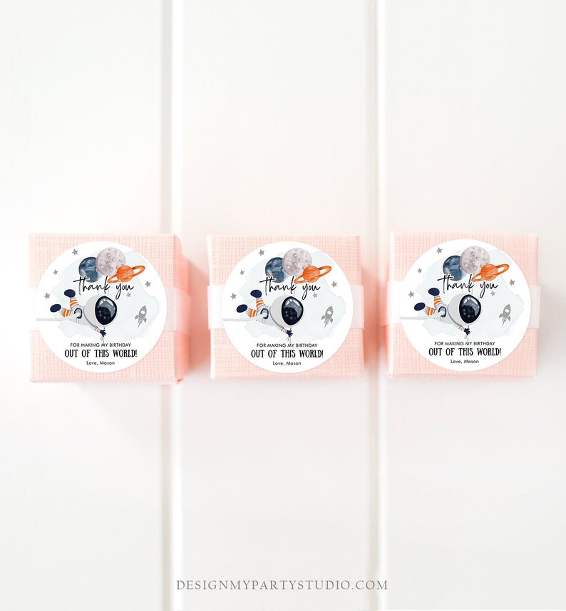Puede incluir: Tres cajas de regalo rosas con etiquetas redondas blancas. Las etiquetas muestran un astronauta de dibujos animados sosteniendo globos con planetas y estrellas. El texto en las etiquetas dice "Gracias" y "Por hacer que mi cumplea&ntilde;os sea fuera de este mundo! Con cari&ntilde;o, Mason".