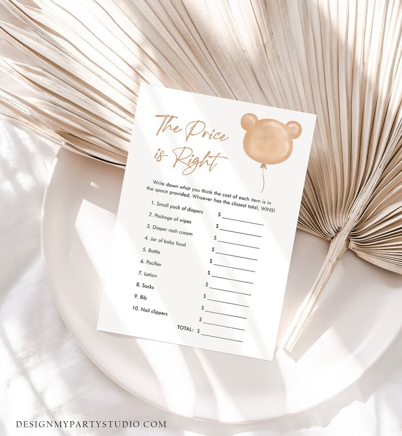 May include: A baby shower game card titled "The Price is Right" with a bear-shaped balloon graphic. The card lists baby items like diapers and lotion, with spaces to write prices. The card is on a white plate with a neutral background.