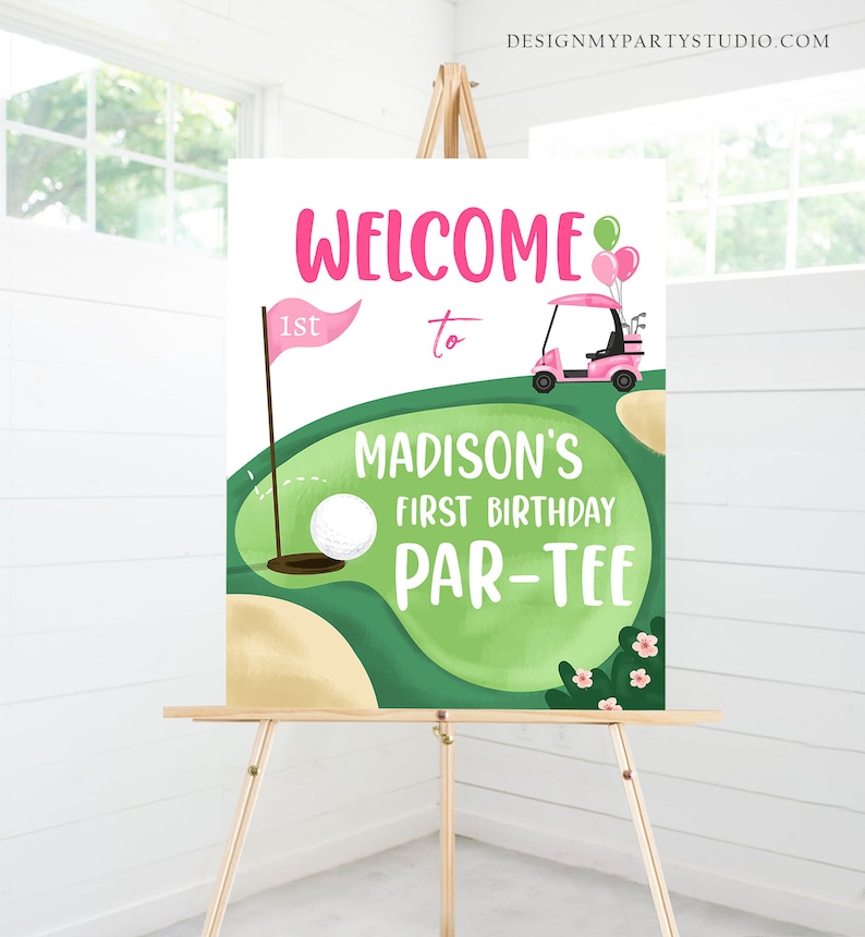 May include: Welcome to Madison's 1st Birthday Par-Tee sign with a green golf course, a pink golf cart, and a golf ball in a hole. The sign is on a wooden easel.