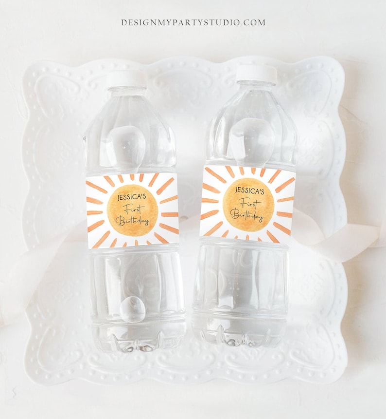 May include: Two clear plastic water bottles with personalized labels. The labels are square and feature a watercolor-style sun with orange and yellow hues. The text on the labels reads "Jessica's First Birthday".