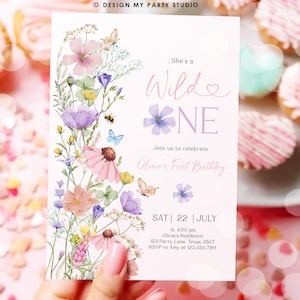 May include: A floral-themed first birthday invitation with a watercolor design featuring pink, purple, and yellow flowers, butterflies, and a bee. The text reads "She's a Wild One" and includes details for the party, including the date, time, location, and RSVP information.