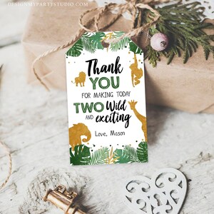 May include: A jungle-themed gift tag with the text "Thank You for making today Two Wild and exciting". The tag features gold animal silhouettes and green foliage. The tag is attached to a wrapped gift.
