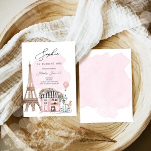 Pode incluir: Um convite em aquarela rosa e branco com tema parisiense. O convite apresenta um desenho da Torre Eiffel, um caf&eacute; e um bal&atilde;o de ar quente. O texto do convite diz "Sophie est&aacute; completando um ano. Junte-se a n&oacute;s para celebrar no s&aacute;bado, 22 de junho &agrave;s 13h. The Cafe 123 Party Lane, Texas 4567 RSVP para Ashley no 123-456-399."