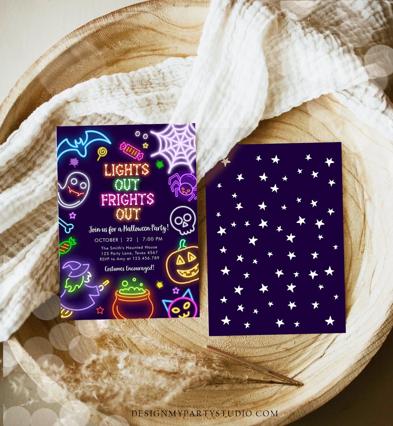 May include: A Halloween party invitation with a neon design. The front features a purple background with Halloween-themed illustrations and the text "LIGHTS OUT FRIGHTS OUT". The back has a dark purple background with white stars. The invitation is on a wooden tray.