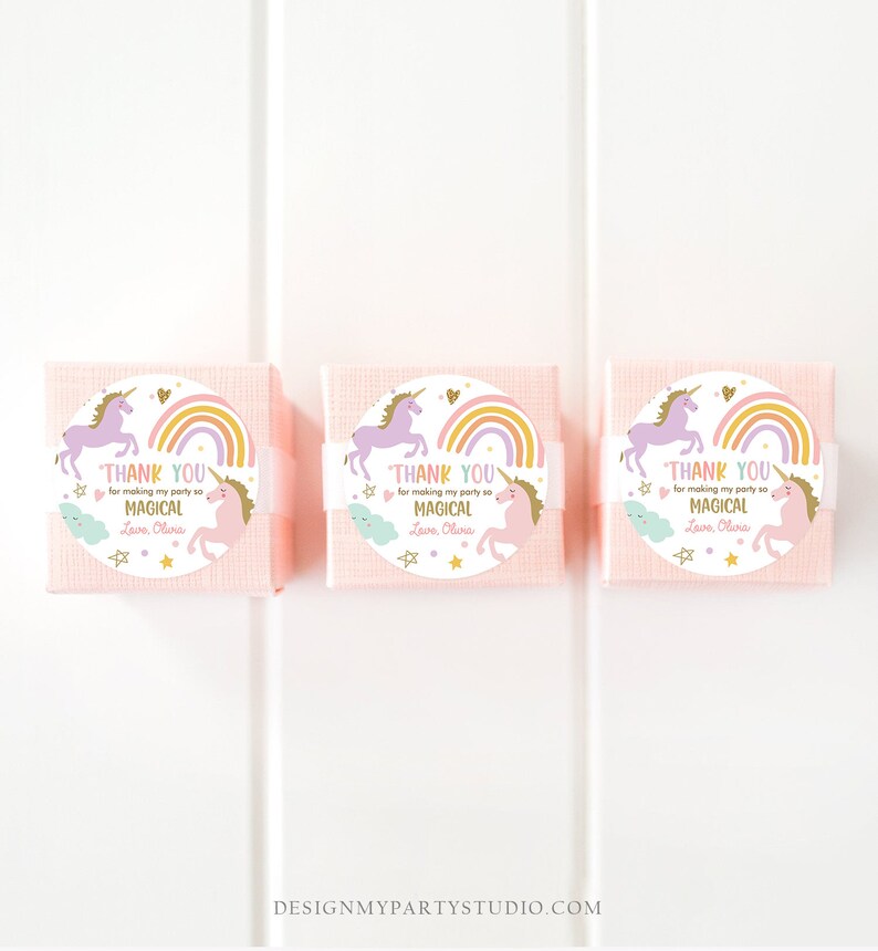May include: Three pink favor boxes with round, white labels featuring a unicorn, rainbow, and stars. The labels say "Thank you for making my party so magical. Love, Olivia."
