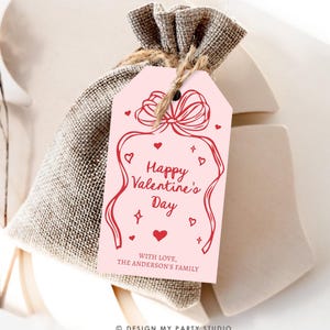 Puede incluir: Etiqueta de regalo rosa para el D&iacute;a de San Valent&iacute;n con una cinta roja y corazones. El texto dice "Feliz D&iacute;a de San Valent&iacute;n" y "Con amor, La familia Anderson".
