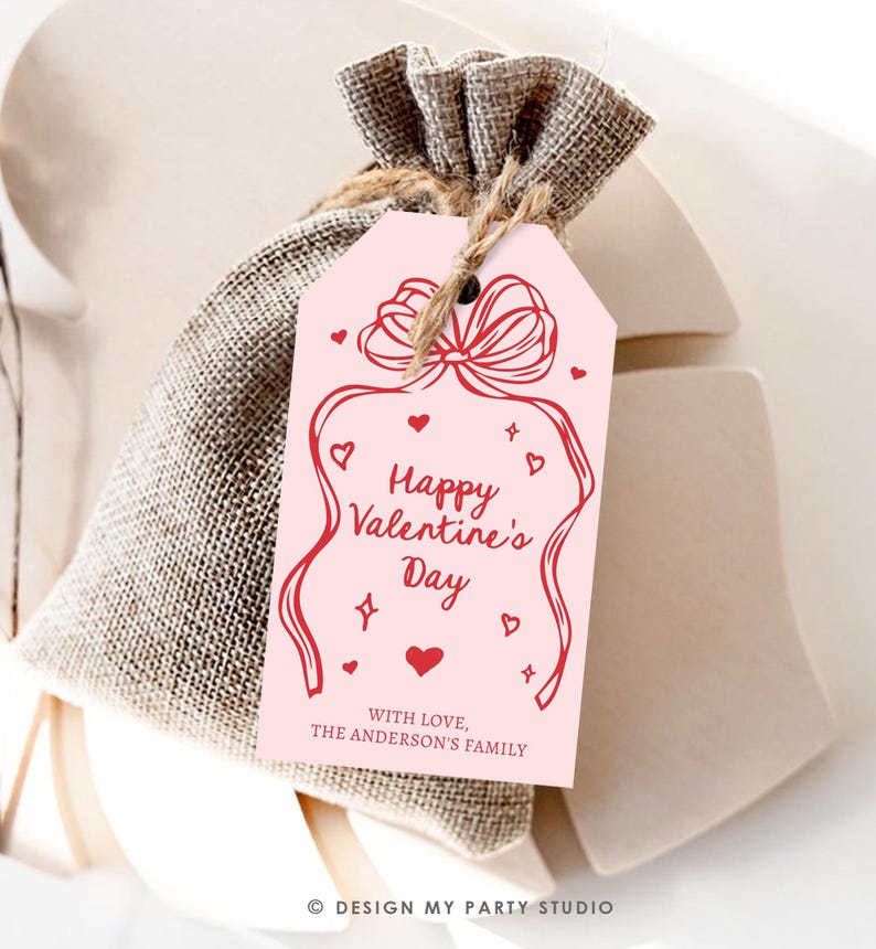 Puede incluir: Etiqueta de regalo rosa para el D&iacute;a de San Valent&iacute;n con una cinta roja y corazones. El texto dice "Feliz D&iacute;a de San Valent&iacute;n" y "Con amor, La familia Anderson".