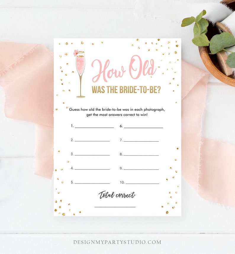 May include: A printable bridal shower game with a pink champagne glass graphic and gold confetti. The game asks guests to guess the bride-to-be's age in each photo. The text reads "How Old Was The Bride-To-Be?"
