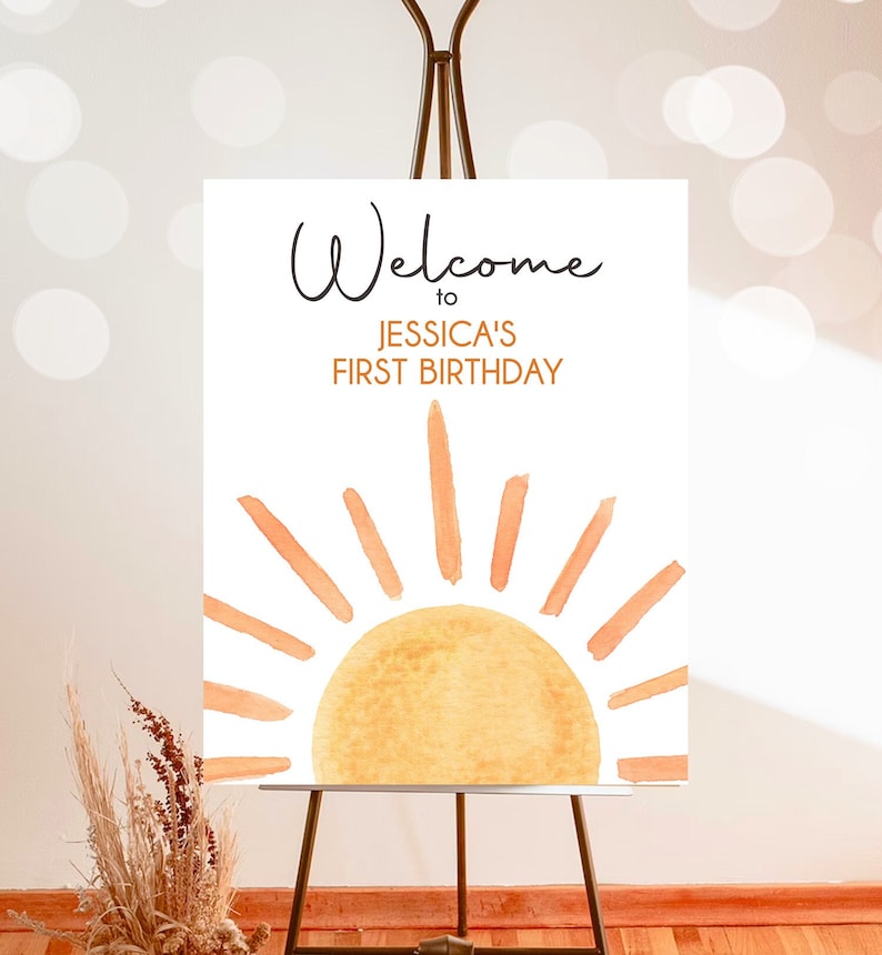 May include: Welcome to Jessica's First Birthday sign with a watercolor illustration of a sun with orange rays on a white background.