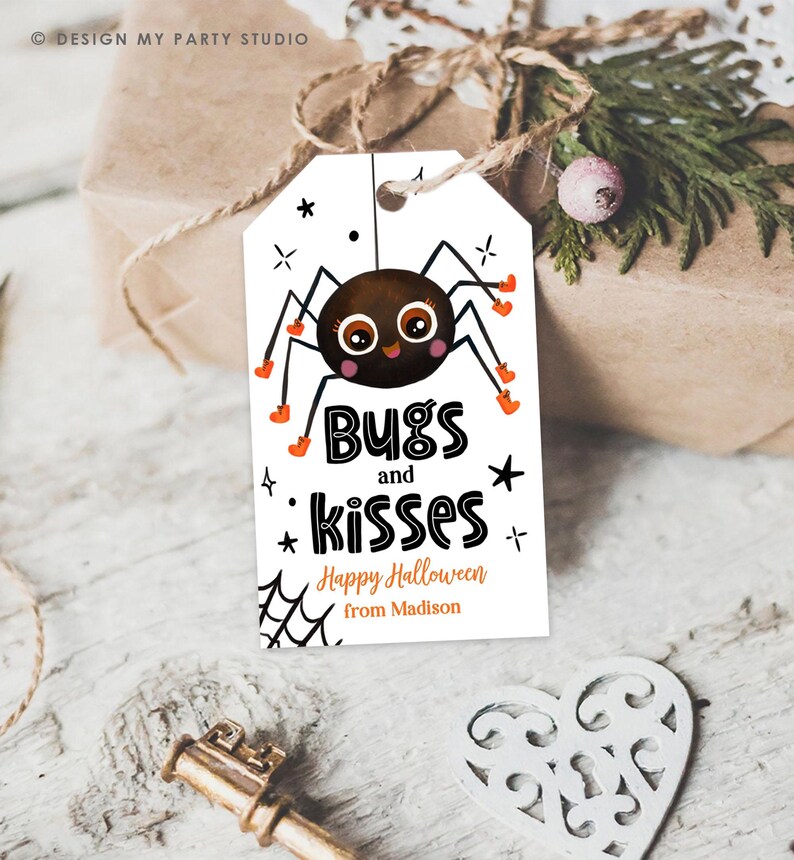 Pu&ograve; includere: Un'etichetta regalo rettangolare bianca con l'illustrazione di un ragno marrone con grandi occhi e accenti arancioni. Il testo recita Bugs and kisses, Happy Halloween e from Madison. Include grafiche di ragnatele e stelle nere.