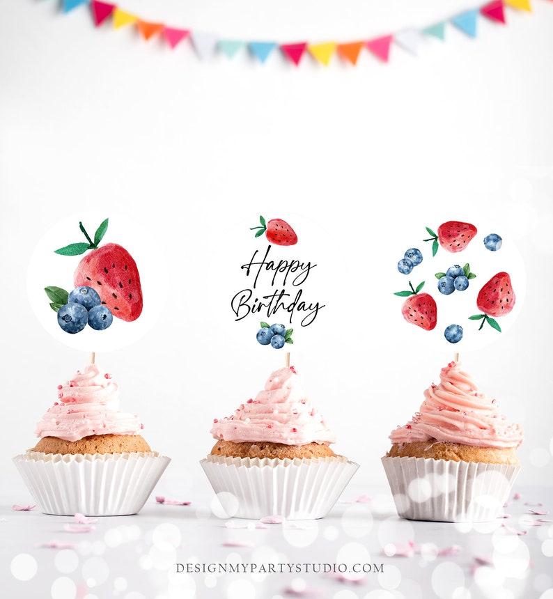 May include: Three pink frosted cupcakes with white cupcake liners. Each cupcake has a different watercolor fruit themed topper. One topper says "Happy Birthday" with blueberries and strawberries. Another topper has a strawberry and blueberries. The last topper has a watermelon and blueberries.