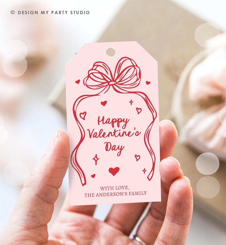 Puede incluir: Etiqueta de regalo rosa con un lazo rojo y el texto "Feliz d&iacute;a de San Valent&iacute;n" y "Con amor, La familia Anderson".